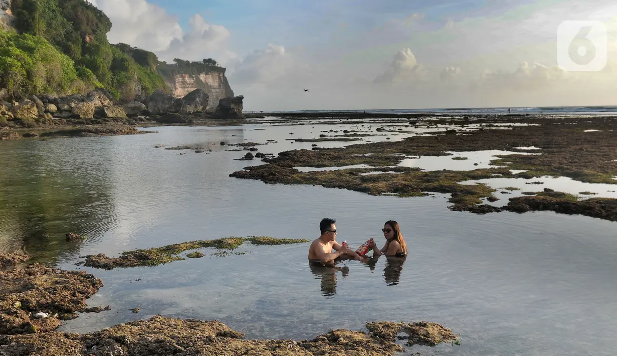 Wisatawan berendam di kolam renang alami yang terbentuk saat air laut surut di kawasan Pantai Suluban, Uluwatu, Bali, Selasa (7/9/2021). Keunikan Pantai Suluban dengan kolam-kolam yang terbentuk di atas karang menjadi daya tarik wisatawan. (merdeka.com/Arie Basuki)