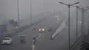 Sejumlah kendaraan melintas di sepanjang jalan di tengah kabut tebal di New Delhi (25/12). India ditetapkan darurat polusi udara. Kualitas udara yang semakin buruk dan kabut beracun menyelimuti. (AFP Photo/Prakash Singh)