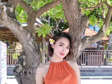 Wika Salim saat berpose di bawah pohon mengenakan dress mini warna oranye model halter. Ia menyelipkan bunga di telinganya agar mempermanis penampilannya. (Instagram/wikasalim)