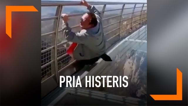 Seorang pria tampak ketakutan saat berada di atas jembatan kaca. Ia tak mampu berdiri dan berteriak histeris meminta pertolongan. Aksinya itu mengundang tawa orang-orang di sekitarnya.