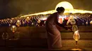 Seorang wanita menyalakan lilin selama perayaan Makha Bucha di kuil Wat Dhammakaya di provinsi Pathum Thani, utara Bangkok (16/2/2022). Hari raya ini dirayakan pada saat bulan purnama di tiap bulan ketiga kalender Buddha. (AFP/Jack Taylor)