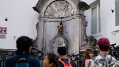 Wisatawan berfoto dekat patung 'Manneken Pis' dalam balutan baju bermotif bunga di ibu kota Belgia, Brussels, Senin (12/8/2019). Patung anak laki-laki yang sedang buang air kecil ini menjadi salah satu daya tarik uta di kota cantik tersebut. (Photo by Kenzo TRIBOUILLARD / AFP)