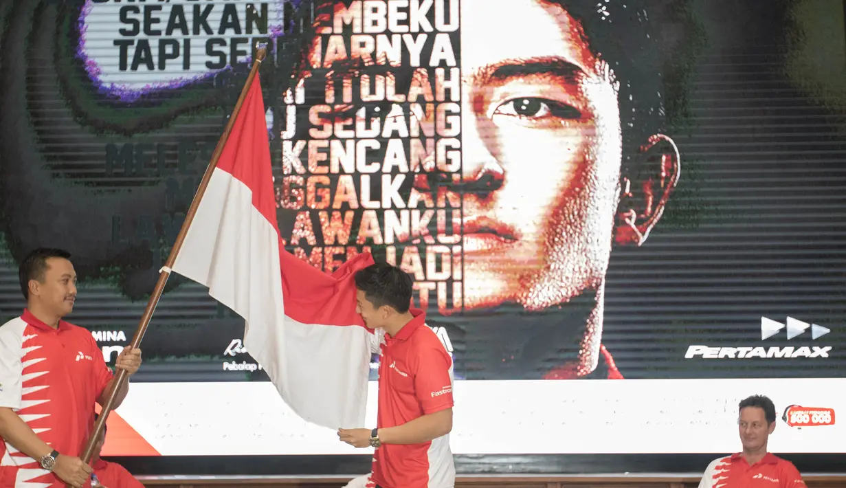 Rio Haryanto mencium bendera merah putih yang dipegang Menpora Imam Nahrawi sesaat setelah resmi diumumkan sebagai pebalap F1 bersama tim Manor Racing di kantor pusat Pertamina, Jakarta, Kamis (18/2/2016). (Bola.com/Vitalis Yogi Trisna)