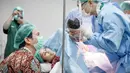 Pada foto lain, seorang dokter memegangi bayi. Dokter berbaju dinas lengkap plus sarung tangan dan penutup kepala memperlihatkan bayi yang baru lahir kepada Gya Sadiqah dan Tarra Budiman. Gya yang mengenakan alat bantu napas tersenyum semringah melibat putri keduanya. Sementara Tarra Budiman yang pakai masker tampak bahagia. Matanya berbinar melihat si kecil. (Foto: Bukaan Moment dari Instagram @gyaps)