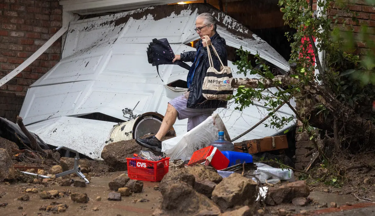 Seorang pria melangkah di atas puing-puing di dekat garasi yang dihantam tanah longsor dan banjir bandang di lingkungan pemukiman, California, pada 5 Februari 2024. (DAVID MCNEW/AFP)