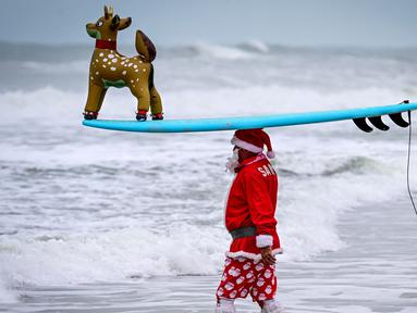 Seorang pengunjung berkostum Sinterklas bersiap untuk berselancar dalam acara Surfing Santa yang berlangsung di Pantai Cocoa, Florida, Amerika Serikat, Selasa (24/12/2024) waktu setempat. (AFP/Giorgio Viera)