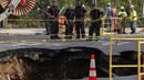 Petugas pemadam kebakaran mengamati  lubang besar (sinkhole) di wilayah Brooklyn, New York, Selasa (4/8/2015). Lubang yang terbentuk di persimpangan pemukiman Sunset Park itu disebabkan erosi dan merusak pipa air serta aspal jalan. (AFP/Kena Betancur)
