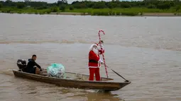 Pada Sabtu 20 Desember 2025, kelompok relawan Sahabat Sinterklas berbagi kebahagiaan Natal untuk untuk anak-anak di komunitas pedesaan dan tepi sungai di hutan hujan Amazon. Tampak dalam foto, relawan Jorge Alberto Barrozo, yang mengenakan kostum Sinterklas, berlayar dengan kano mengantarkan hadiah kepada anak-anak di komunitas tepi sungai di daerah pedesaan Careiro da Varzea, negara bagian Amazonas, Brasil pada Sabtu 20 Desember 2025. (Michael DANTAS/AFP)