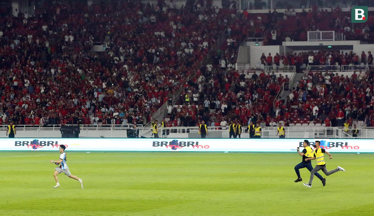 Petugas keamanan mengejar seorang suporter yang masuk kedalam lapangan dan berlari ke arah pemain Timnas Argentina setelah laga FIFA Matchday antara Timnas Indonesia Vs Timnas Argentina di Stadion Utama Gelora Bung Karno (SUGBK), Senayan, Jakarta, Senin (19/06/2023). (Bola.com/M Iqbal Ichsan)