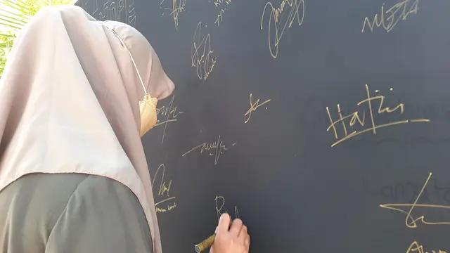 Seorang pengunjung "Letter of Hope" sedang membubuhi tanda tangan di atas kain hitam yang dibentang di halaman KontraS Aceh, Sabtu (13/8/2022), (Liputan6.com/Rino Abonita)