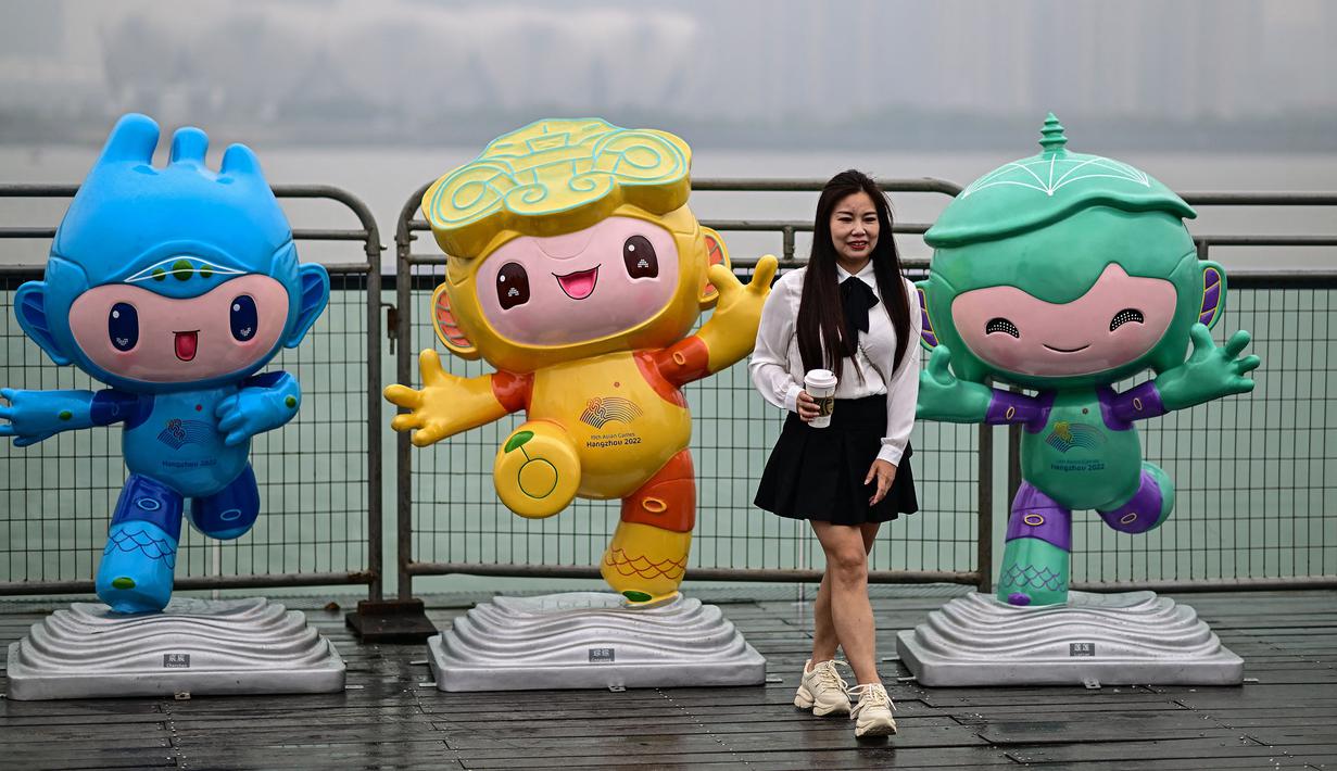 Seorang wanita berpose di antara maskot Asian Games 2022 (Chenchen, Congcong, dan Lianlian) yang terletak di sepanjang Sungai Qiantang di Hangzhou, Zhejiang, China pada 22 September 2023 waktu setempat. (AFP/Manan Vatsyayana)