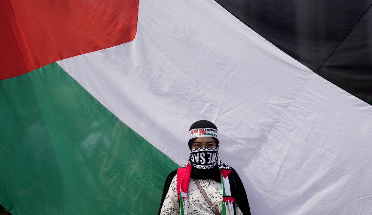 Seorang perempuan berdiri di depan bendera besar Palestina saat aksi bela Palestina, di Monumen Nasional atau Monas, Jakarta Pusat, Minggu (5/11/2023). (AP Photo/Dita Alangkara)