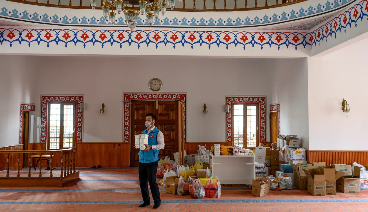Imam masjid Dedeman, Abdulsamet Cakir (33) membawa barang-barang menuju pintu masjid di distrik Sariyer, Istanbul pada 21 April 2020. Di pintu masuk masjid itu dimana rak-rak yang biasanya diperuntukkan sebagai tempat sepatu jemaah, kini penuh dengan kebutuhan sehari-hari. (Bulent Kilic/AFP)