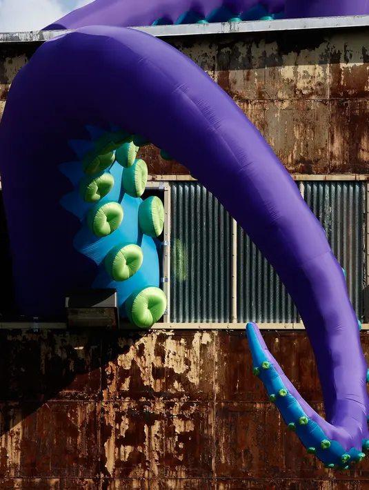 Sebuah patung karet berjudul "Sea Monsters HERE" menghiasi gudang berkarat Building 61 di Navy Yard di Philadelphia, Selasa (9/10). Kreasi sepanjang 40 kaki ini menampilkan tentakel ungu besar yang keluar dari jendela hingga ke atap. (AP/Matt Rourke)