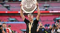 Kiper Arsenal, Aaron Ramsdale, berpose dengan trofi Community Shield setelah The Gunners memenangi duel kontra Man City di Wembley Stadium, Minggu (6/8/2023). Arsenal menang 4-1 lewat adu penalti setelah bermain imbang 1-1 dalam waktu normal. (Glyn KIRK/AFP)