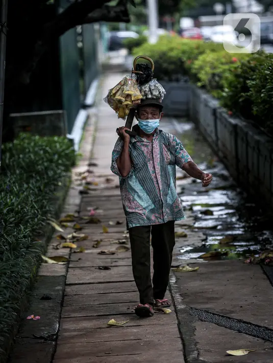 Seorang pedagang berjalan di Kawasan Sudirman, Jakarta, Kamis, (17/2/2022). Kepala BPBD DKI Jakarta Isnawa Adji mengatakan, Menteri Kesehatan (Menkes) Budi Gunadi Sadikin sudah memberikan sinyal bahwa DKI telah melewati pandemi gelombang ketiga. (Liputan6.com/Faizal Fanani)