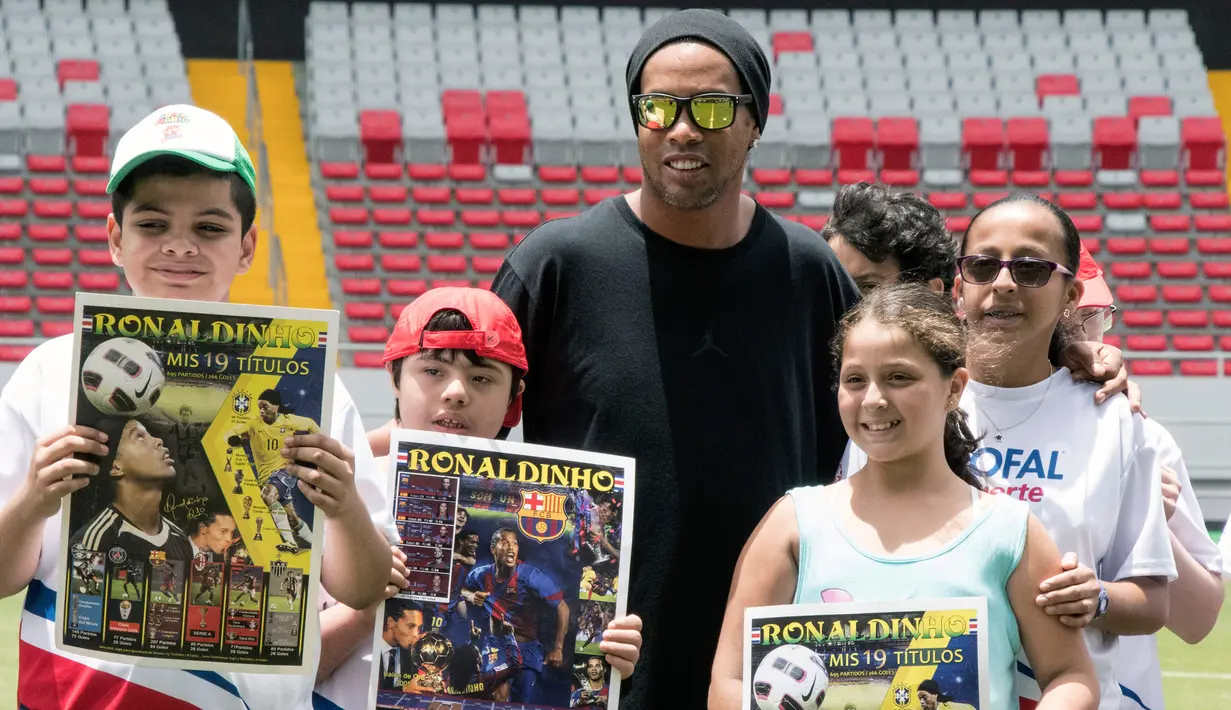 Mantan bintang sepak bola Brasil Ronaldinho berpose dengan anak-anak Kosta Rika sebelum pertandingan persahabatan melawan mantan pemain Kosta Rika di Stadion Nasional di San Jose, (4/8). (AFP Photo/Ezequiel Becerra)