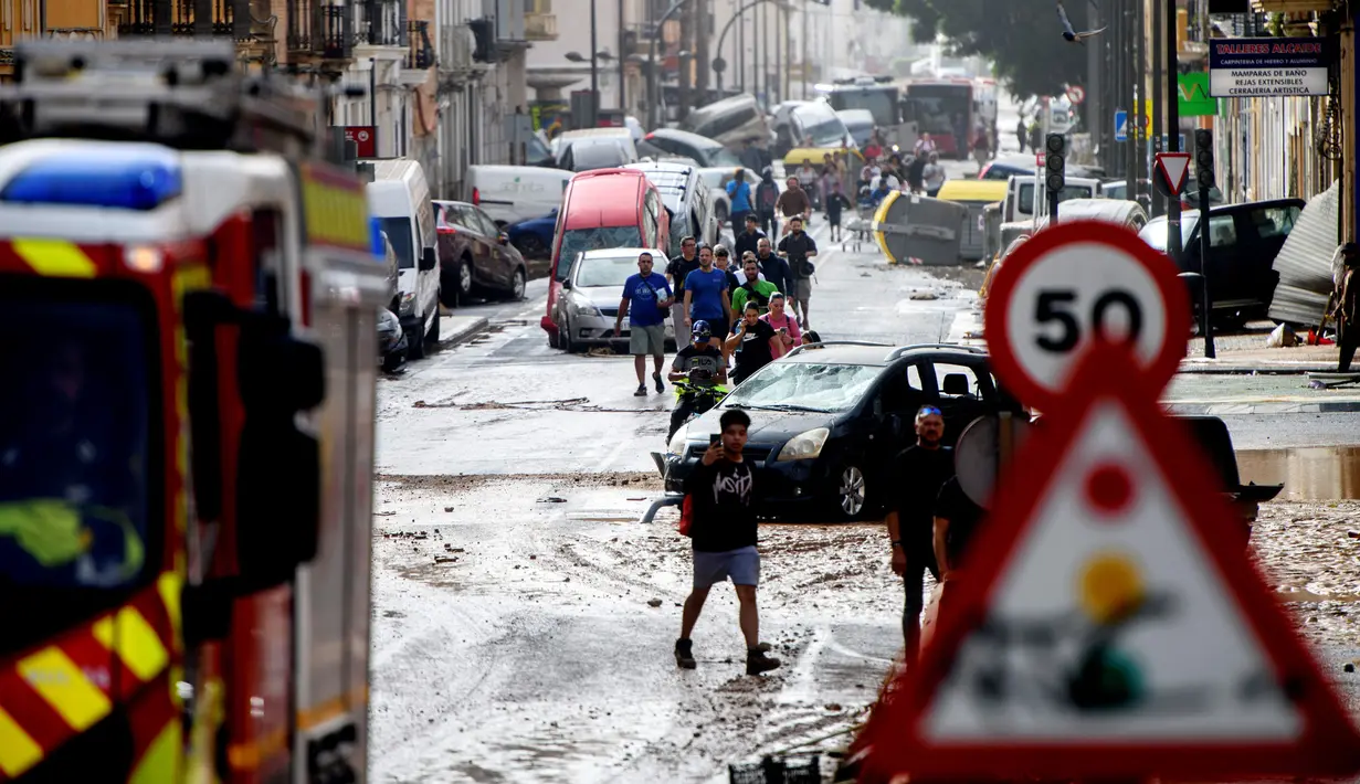Warga berjalan di samping tumpukan mobil di sebuah jalan yang tertutup lumpur setelah banjir di kawasan De La Torre, Valencia, Spanyol timur, pada tanggal 30 Oktober 2024. (Ruben FENOLLOSA/AFP)