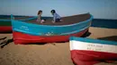 Dua anak  mengenakan masker duduk di atas sebuah kapal ketika penguncian untuk memerangi penyebaran virus corona berlanjut di sebuah pantai di Badalona, dekat Barcelona, Spanyol, Selasa, (28/4/2020).  (AP Photo/Emilio Morenatti)