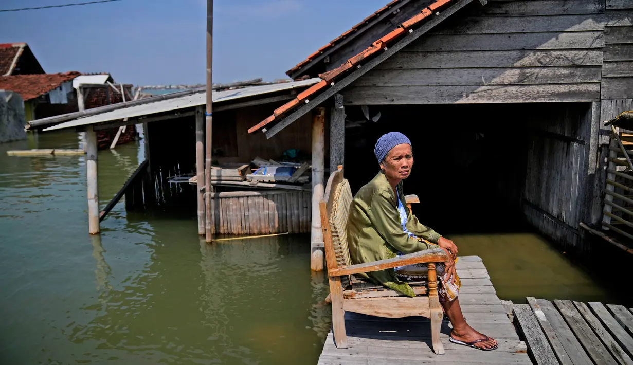 Mar'iah duduk di luar rumahnya sambil menunggu air banjir surut di Timbulsloko, Jawa Tengah, Indonesia, 31 Juli 2022. Mar'iah menjelaskan bahwa dia duduk di kursi setiap hari menunggu sampai rumahnya cukup kering untuk masuk lagi. (AP Photo/Dita Alangkara)