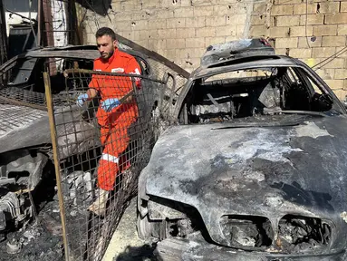 Seorang petugas medis berdiri di samping puing-puing mobil di kamp pengungsi Palestina Ain al-Hilweh, dekat Sidon di selatan Lebanon, pada Rabu 19 November 2025. Sebuah serangan udara Israel menghantam kamp pengungsi Palestina Ain al-Hilweh di Lebanon selatan. (Mahmoud ZAYYAT/AFP)