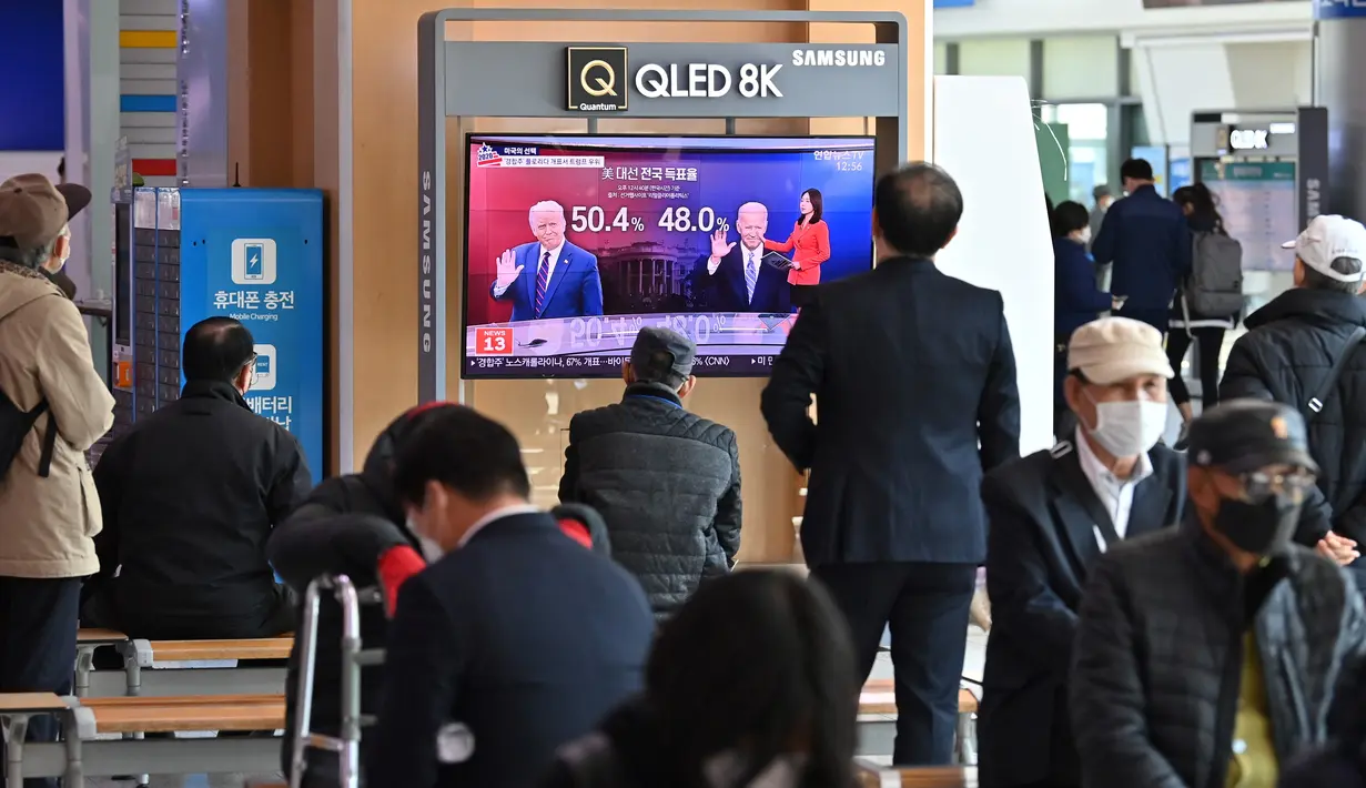 Orang-orang menonton program berita televisi tentang pemilihan presiden (pilpres) AS yang menampilkan gambar Presiden Donald Trump (kiri) dan calon presiden dari Partai Demokrat Joe Biden (kanan), di sebuah stasiun kereta api di Seoul, Korea Selatan pada Rabu (4/11/2020). (Photo by Jung Yeon-je/AFP)