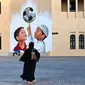 Seorang wanita berjalan melewati mural di Doha, Qatar pada 8 November 2022, menjelang turnamen sepak bola Piala Dunia 2022. (Gabriel BOUYS/AFP)
