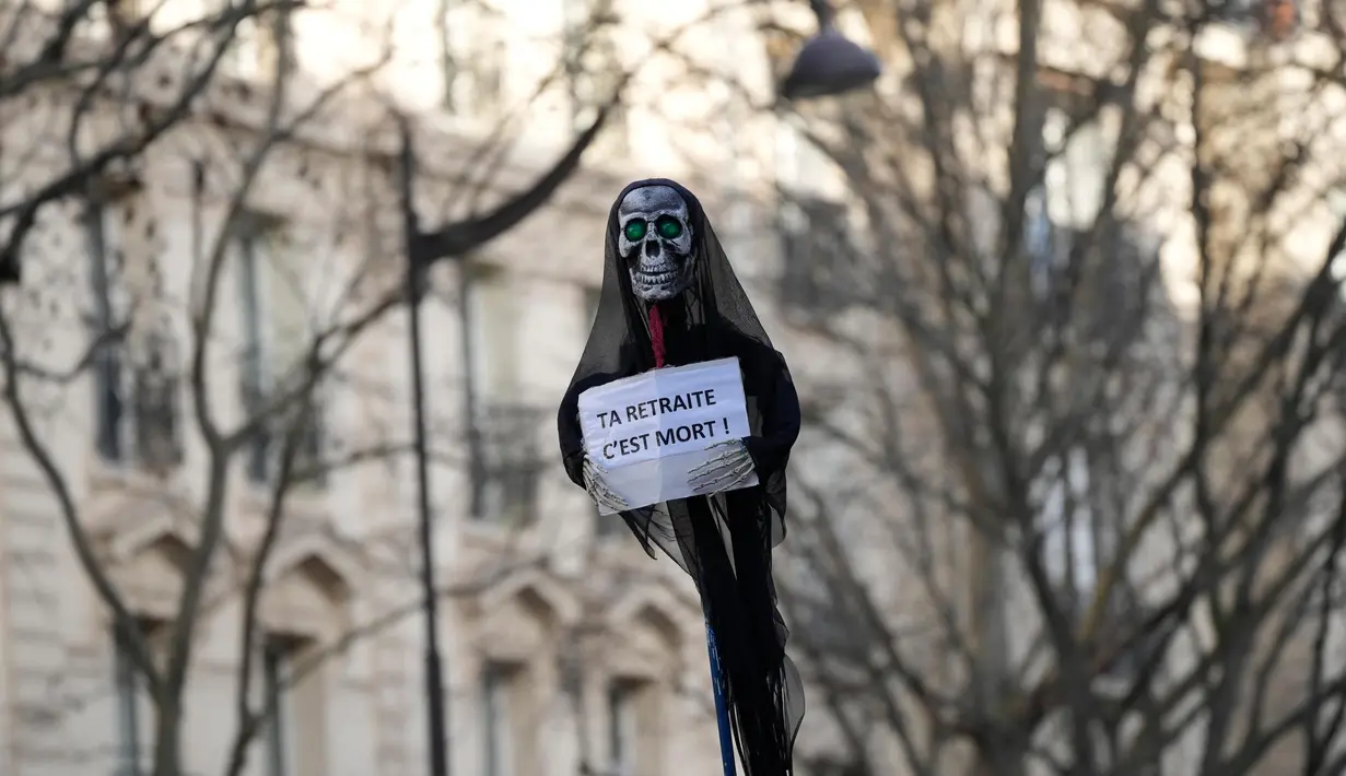 Seorang pengunjuk rasa memegang simbol kematian dengan poster bertuliskan "pensiun Anda sudah mati" selama demonstrasi menentang rencana untuk memundurkan usia pensiun di Prancis, Paris, Selasa (31/1/2023). Jutaan demonstran kembali turun ke jalan untuk memprotes rencana Presiden Emmanuel Macron menaikkan usia pensiun, dari yang sebelumnya 62 tahun menjadi 64 tahun. (AP Photo/Christophe Ena)