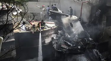 Petugas pemadam kebakaran menyemprotkan air pada puing pesawat Pakistan International Airlines yang jatuh di Karachi, Pakistan, Jumat (22/5/2020). Menurut perwakilan dari Kementerian Kesehatan Sindh, 97 orang dilaporkan meninggal dan dua orang selamat dalam kecelakaan tersebut. (Rizwan TABASSUM/AFP)