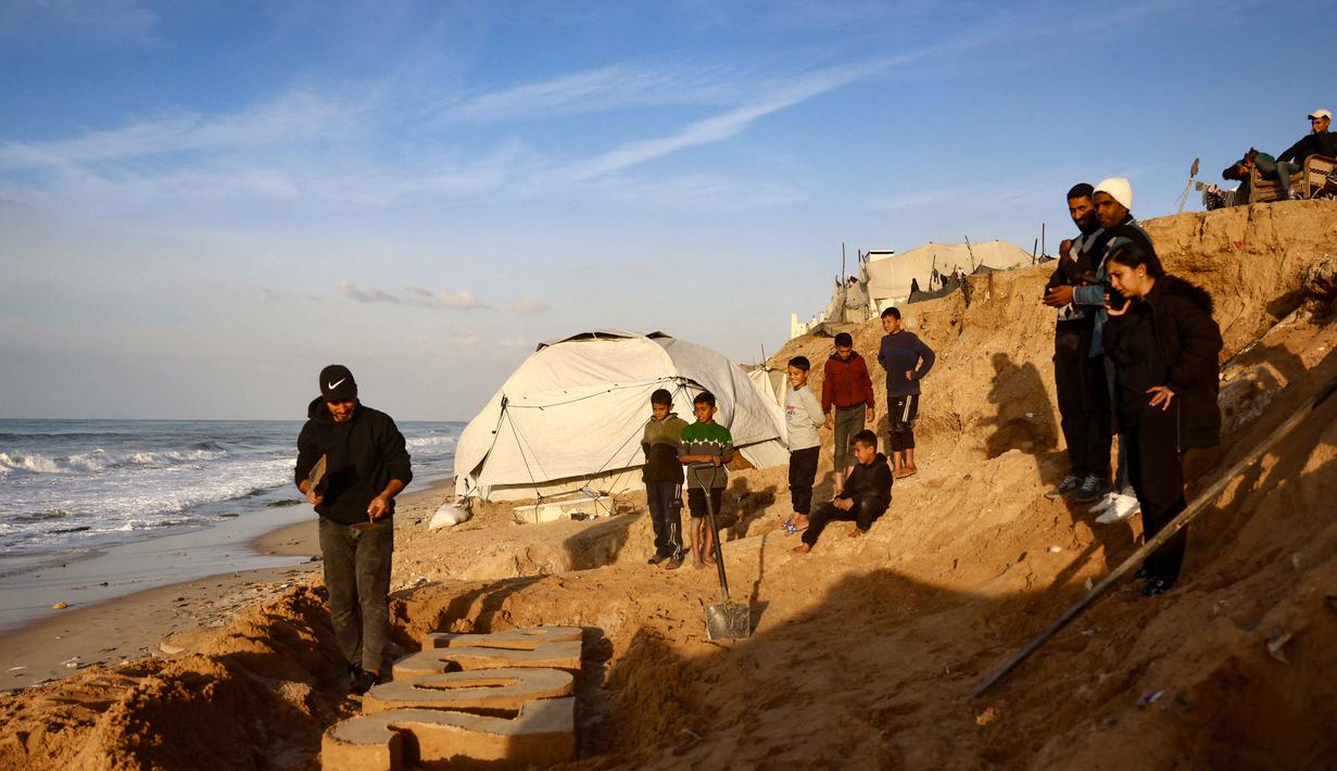 Memasuki detik-detik pergantian tahun, krisis kemanusiaan di Jalur Gaza masih sangat memprihatinkan. Tampak dalam foto, warga menyaksikan seniman Yazed Abo Jarad membuat patung pasir untuk tahun mendatang di Deir El-Balah, Jalur Gaza tengah pada 30 Desember 2025. (Bashar Taleb/AFP)