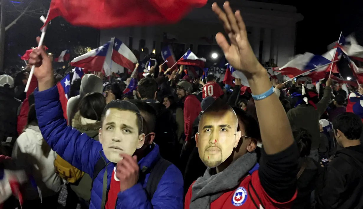 Suporter Chili berkumpul di jalan memakai topeng Alexis Sanchez (kiri) dan Arturo Vidal merayakan kemenangan Chili atas Peru di Copa Amerika 2015 di kota Santiago, (29/6/2015). Chile melaju ke final usai mengalahkan Peru 2-1. (REUTERS/Jorge Adorno)
