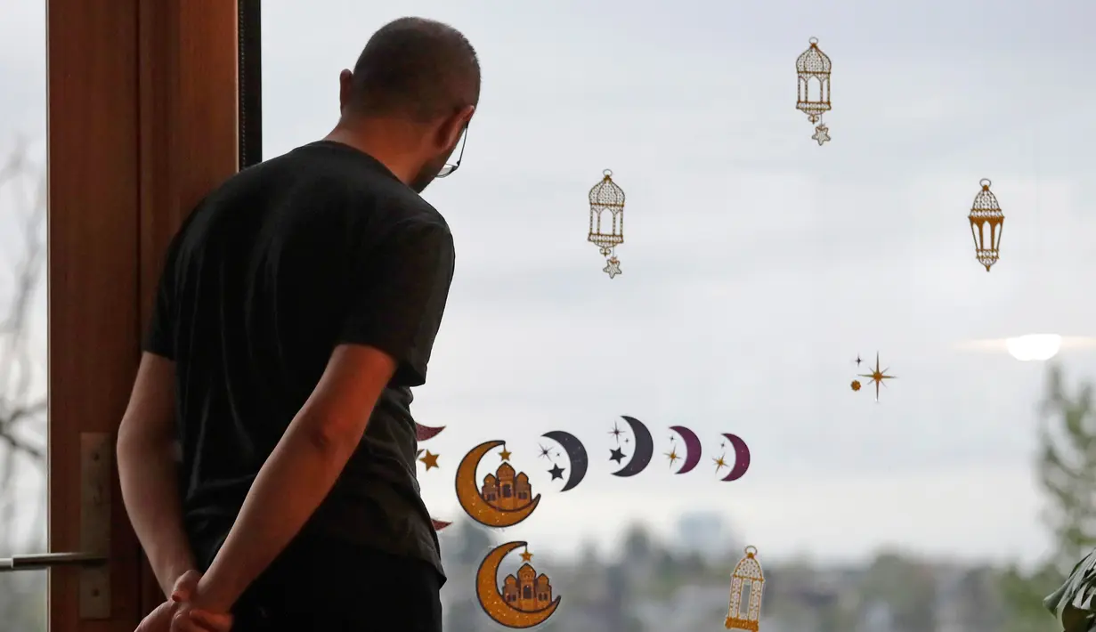 Ahmad Kamel melihat ke barat, menunggu matahari terbenam sementara stiker Ramadan menghiasi jendela di sebelahnya ketika ia dan keluarganya menunggu untuk berbuka puasa Ramadan di rumah keluarganya di tengah wabah coronavirus di Seattle (28/4/2020). (AP/Elaine Thompson)