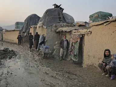Seorang pria Afghanistan duduk di dinding ketika yang lain berjalan melalui jalan berlumpur di sebuah kamp di Kabul, Afghanistan (27/11/2019). Puluhan ribu warga Afghanistan yang terlantar secara internal tinggal di kamp-kamp, yang kekurangan fasilitas dasar, di Afghanistan. (AP Photo/Altaf Qadri)