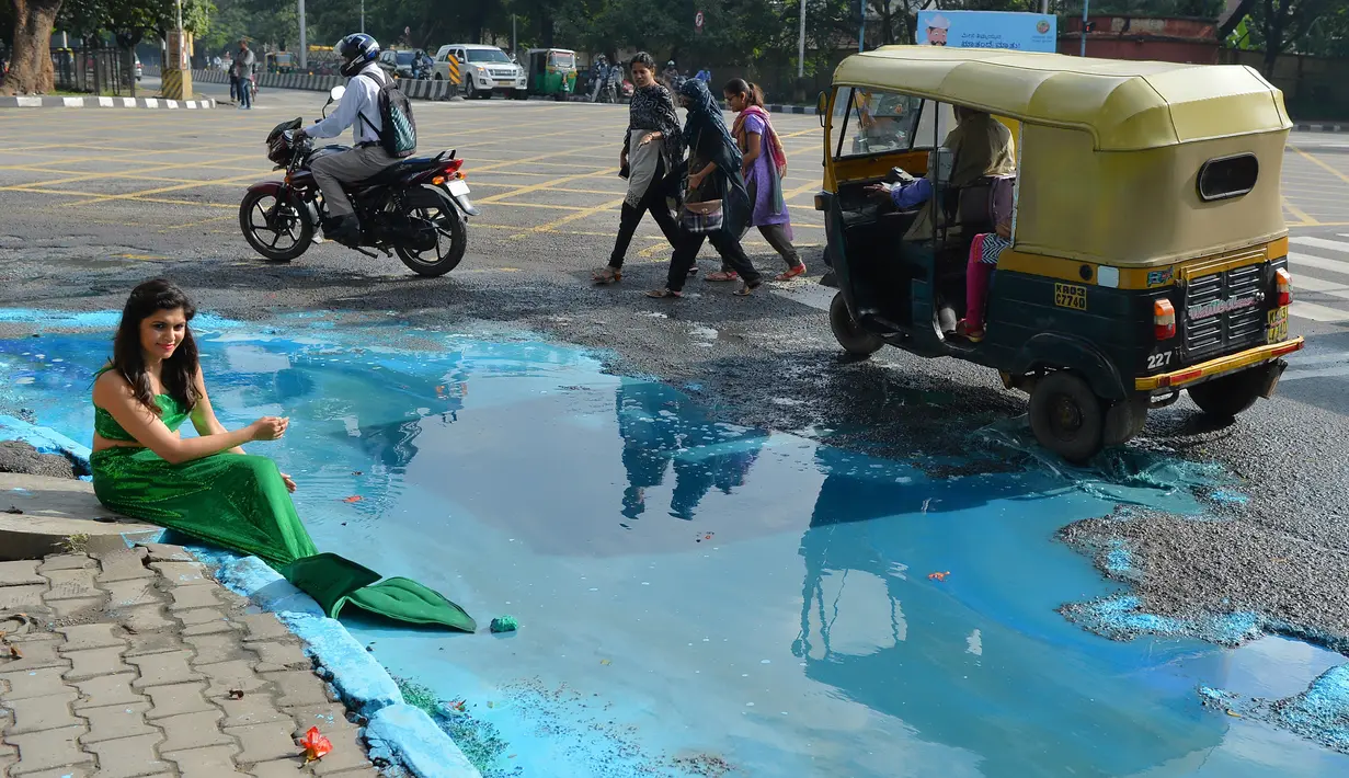 Model berpakaian putri duyung ambil bagian dalam seni instalasi seniman Baadal Nanjundawsamy di Bangalore, India, 13 Oktober 2107. Karya seni itu menunjukkan lubang besar di jalan-jalan tersebut yang luput dari perhatian pemerintah (MANJUNATH KIRAN / AFP)