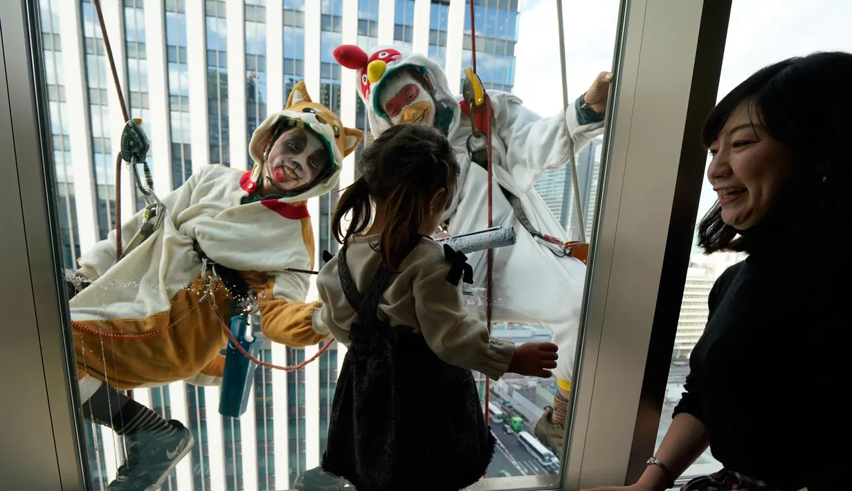 Seorang anak melihat pembersih jendela wanita berkostum ayam jago dan anjing di kawasan perbelanjaan dan bisnis Tokyo, Jepang (20/12). Ayam jago merupakan binatang zodiak tahun ini dan anjing untuk tahun depan. (AP Photo / Shizuo Kambayashi)