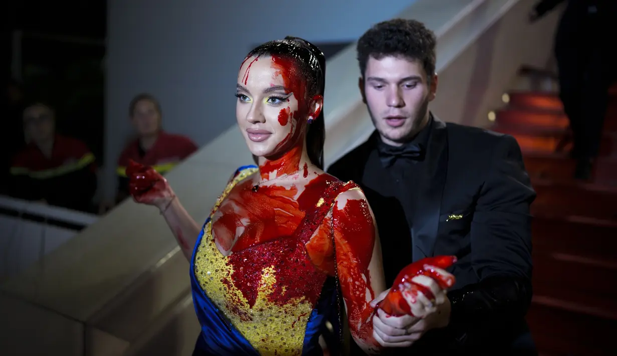 Disiram dengan darah palsu, perempuan itu tampak tidak terpengaruh saat diseret keluar dari karpet merah. (AP Photo/Daniel Cole)