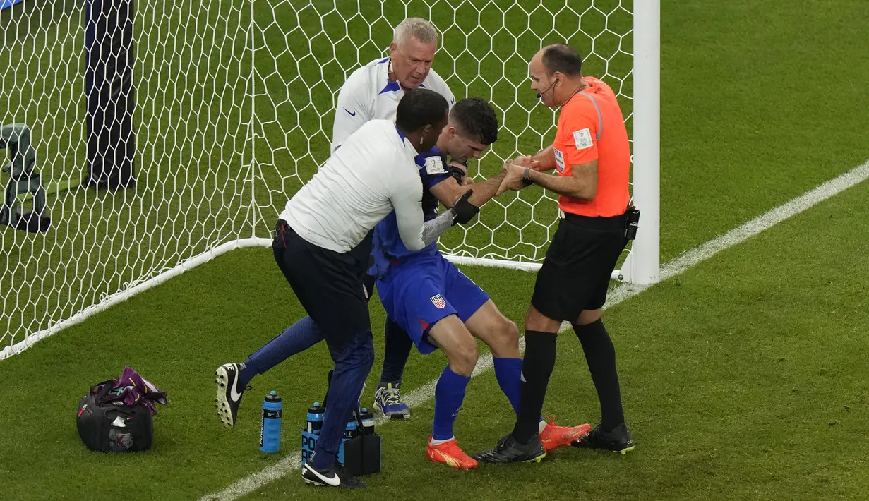 Gelandang Amerika Serikat Christian Pulisic dibantu  wasit Antonio Mateu dan tim dokter setelah cedera karena bertabrakan dengan kiper Iran Alireza Beiranvand pada laga pamungkas Grup B Piala Dunia 2022 di Stadion Al Thumama, Rabu (30/11/2022) dini hari WIB. Pulisic dilarikan ke rumah sakit setelah mengeluh pusing dan sakit perut. (AP Photo/Luca Bruno)
