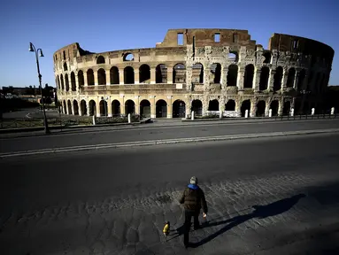 Seorang pria membawa anjingnya jalan-jalan di depan Colosseum, Roma, Italia, 3 April 2020. Menurut Departemen Perlindungan Sipil Italia pada 6 April 2020, jumlah kasus virus corona COVID-19 di negara tersebut menjadi 132.547 infeksi, 16.523 meninggal, dan 22.837 sembuh. (Filippo MONTEFORTE/AFP)