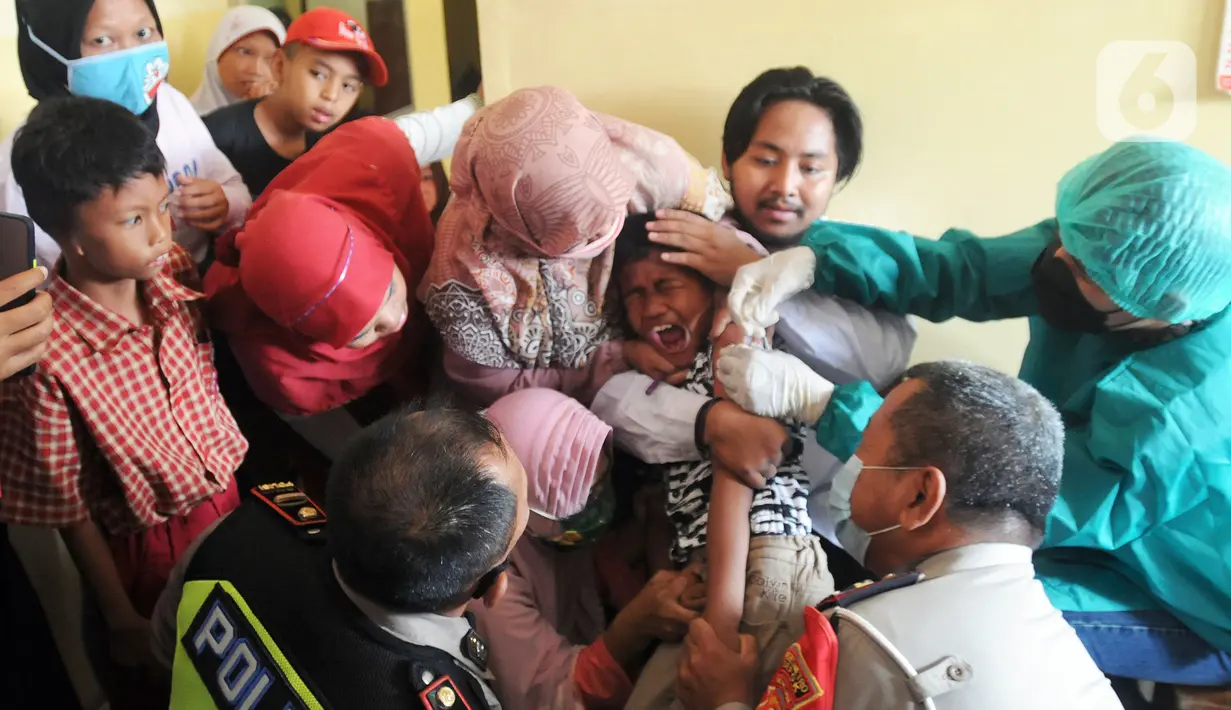 Anggota Polri dari Polsek Cinere memegangi murid penyandang tunagrahita saat disuntik vaksin COVID-19 di SLB BC Manunggal Bhakti, Depok, Selasa (11/1/2022). Delapan murid SLB disuntik vaksin COVID-19 Sinovac yang merupakan rangkaian program Vaksinasi Merdeka. (merdeka.com/Arie Basuki)
