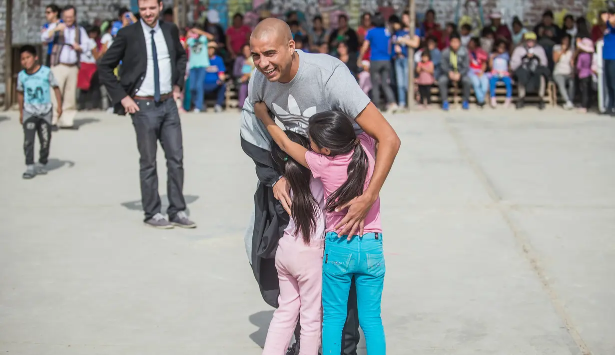 Mantan pemain bola Juventus, David Trezeguet memeluk dua gadis kecil di komunitas San Pablo Mirador, Peru (13/7). Trezeguet melakukan kunjungan ke Peru untuk mempromosikan Paris yang menjadi tuan rumah Olimpiade 2024. (AFP Photo/Ernesto Benavides)