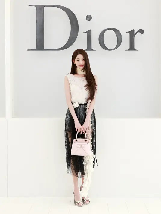 Jang Wonyoung tampil playful dengan atasan lace krem berlengan cap dan rok lace hitam bertumpuk. Dilengkapi syal mutiara di leher, tas Dior Cigale soft pink , dan heels pita keemasan [dok. Dior]
