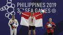 Lifter Aisyah Windy mengibarkan bendera saat naik podium usai mendapatkan medali emas SEA Games 2019 cabang angkat besi nomor 49 kg di Stadion Rizal Memorial, Manila, Minggu (1/12). Dirinya meraih emas dengan total angkatan 104 kg. (Bola.com/M Iqbal Ichsa