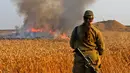 Tentara wanita Israel melihat kebakaran yang terjadi di ladang gandum dekat Kibbutz of Mefallesim di perbatasan Jalur Gaza (15/5). Sebelumnya telah terjadi bentrokan antara warga Palestina dan tentara Israel di Jalur Gaza. (AFP/Jack Guez)