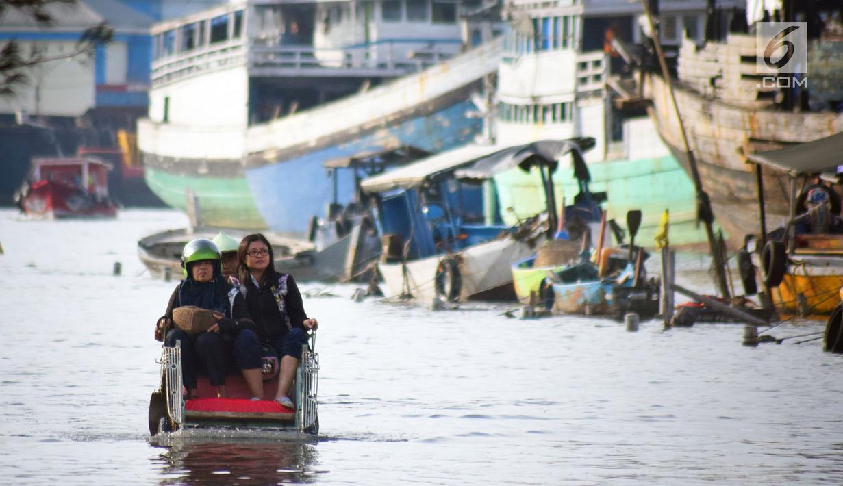 Warga menaiki becak untuk melintasi banjir rob di jalan Yos Sudarso Semarang di kawasan Pelabuhan Tanjung Emas (24/4). Banjir rob ini terjadi karena dipicu oleh salah satunya sistem drainase yang masih kurang baik. (Liputan6.com/Gholib)
