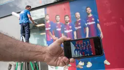Seorang pria menunjukkan foto di ponselnya yang menampilkan poster pemain depan Barcelona Neymar (kedua kanan) sebelum diganti dengan poster yang terbaru di luar Stadion Camp Nou di Barcelona (2/8). (AFP Photo/Josep Lago)