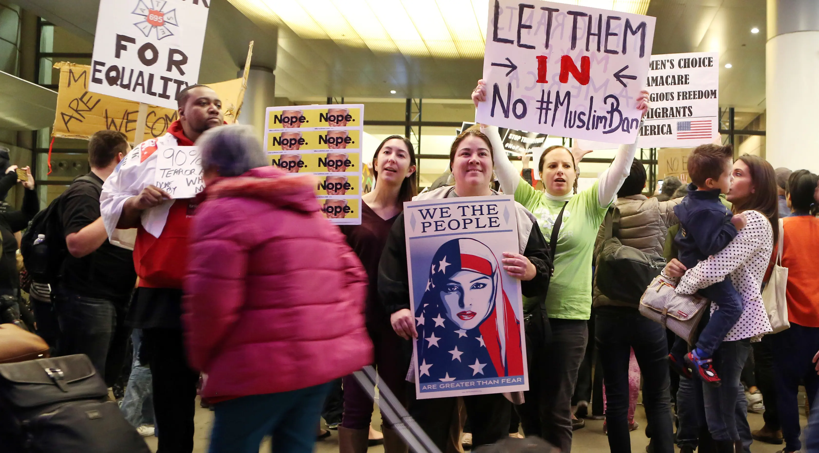 Calon penumpang melewati massa yang menggelar aksi protes di Terminal Internasional Tom Bradley, Bandara LAX, Los Angeles, Sabtu (28/1). Mereka menggelar aksi protes terkait kebijakan Presiden AS Donald Trump tentang imigrasi. (AP Photo/Reed Saxon)