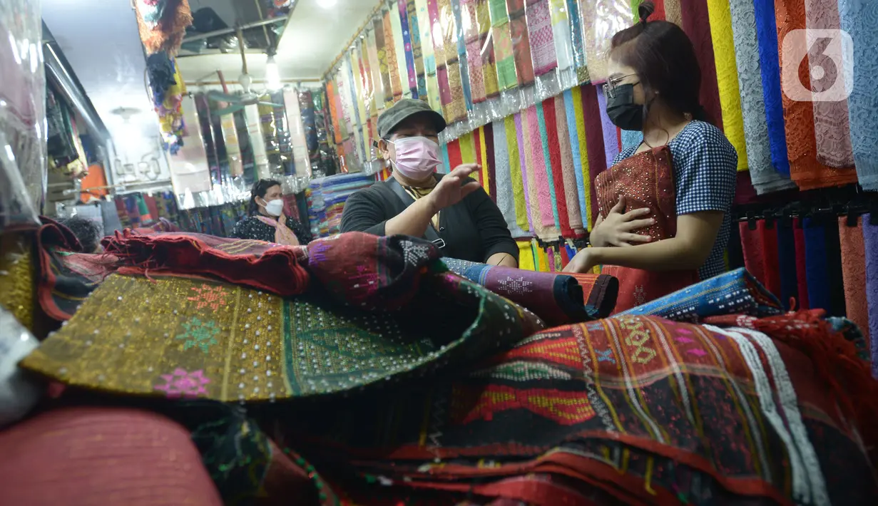 Aktivitas jual beli kain ulos di pasar proyek Senen, Jakarta, Kamis (21/10/2021). Sejak status PPKM turun dari level 3 menjadi level 2, pengunjung ramai mendatangi toko membeli kain ulos untuk upacara pernikahan adat dengan kisaran harga dari Rp. 500.000 hingga jutaan rupiah. (merdeka.com/Imam Buhor