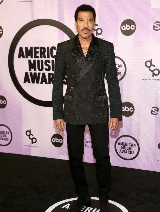<p>Lionel Richie terlihat tampan dalam balutan blazer hitam bercorak bunga. Ia padukan dengan celana dan sepatu yang juga berwarna hitam. Foto: Vogue.</p>