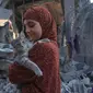 Seorang anak perempuan Palestina menggendong seekor kucing saat dia memeriksa kerusakan setelah pemboman Israel di Rafah di Jalur Gaza selatan, pada 18 Oktober 2023. (SAID KHATIB/AFP)