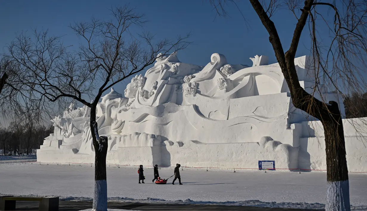 Orang-orang berjalan di samping patung salju raksasa di Pameran Seni Patung Salju Internasional Harbin Sun Island menjelang Festival Es dan Salju Internasional Harbin Tiongkok ke-39 di Harbin, di provinsi Heilongjiang timur laut China (4/1/2023). (AFP/Hector Retamal)